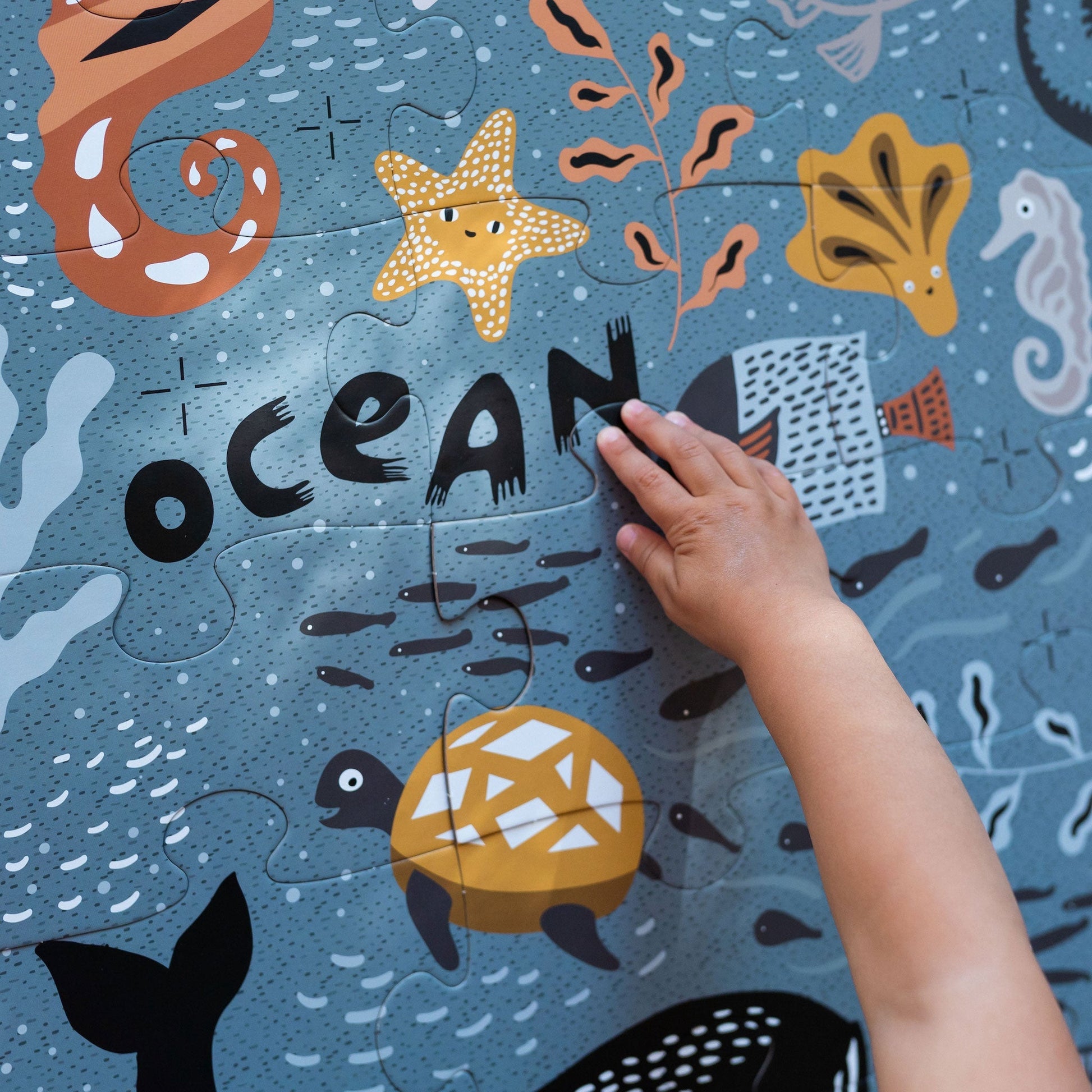 Children's puzzle with ocean-themed design and a hand placing a piece.