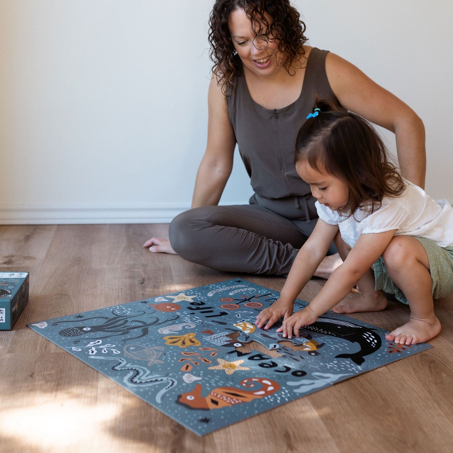 Woman and child playing with an educational mat on a wooden floor.