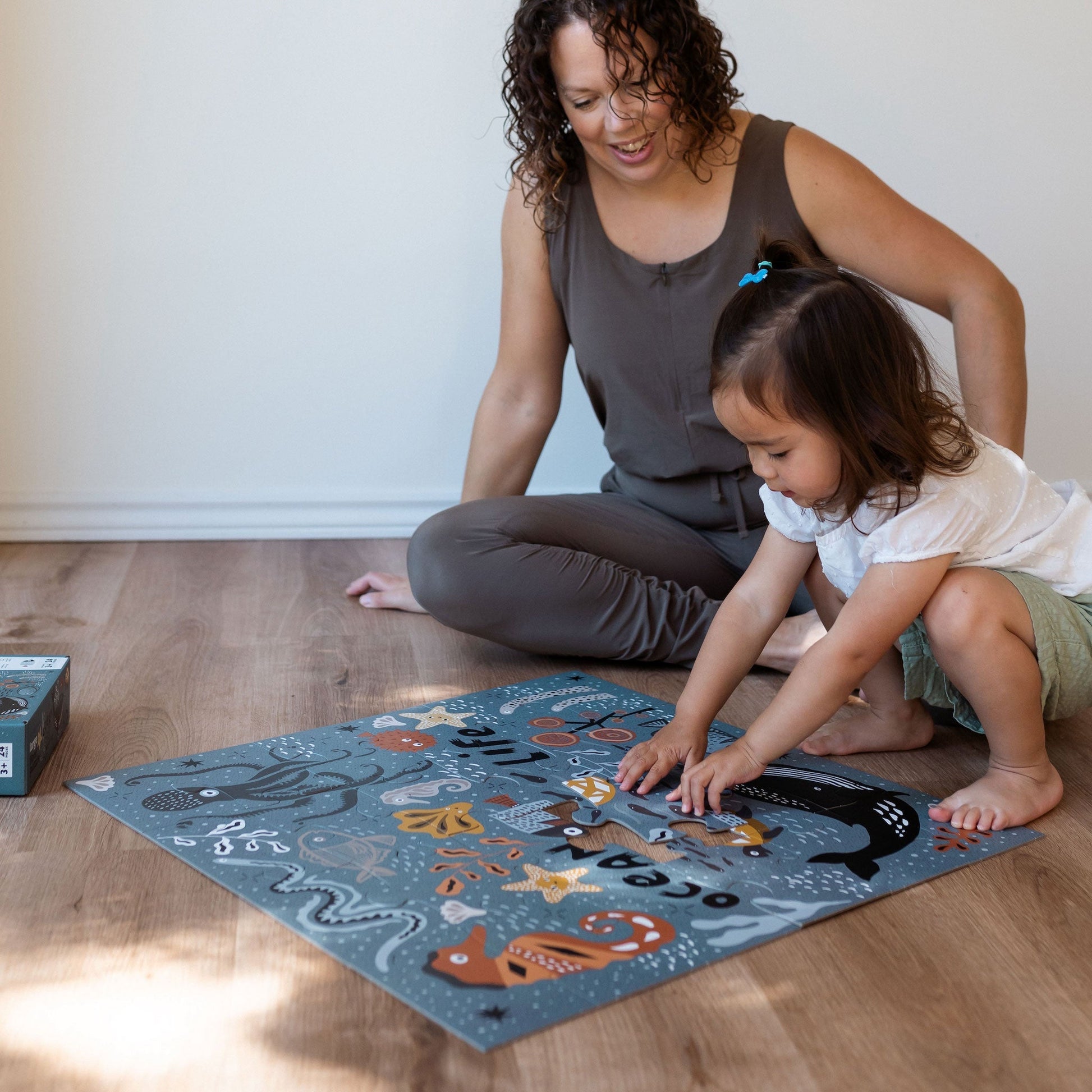 Woman and child playing with an educational mat on a wooden floor.