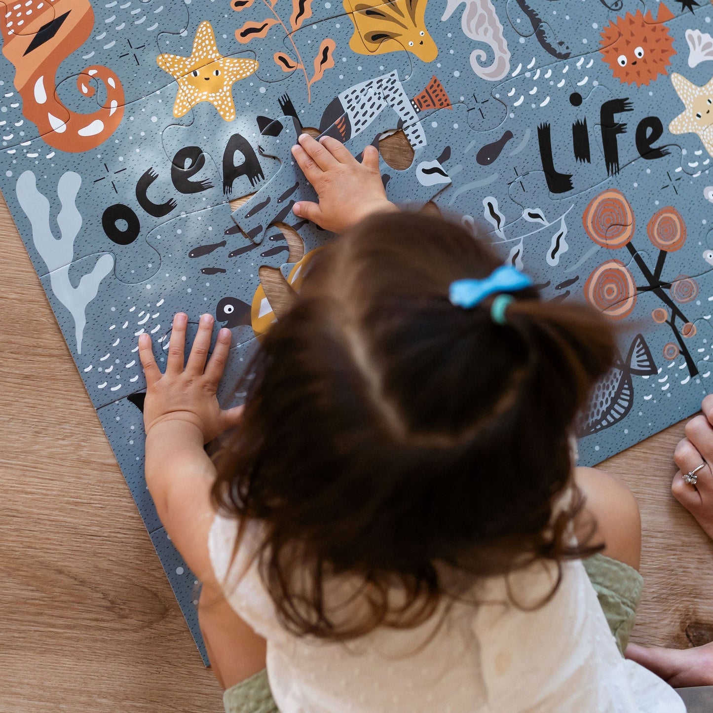 Child playing with an 'Ocean Life' themed puzzle on a wooden floor.