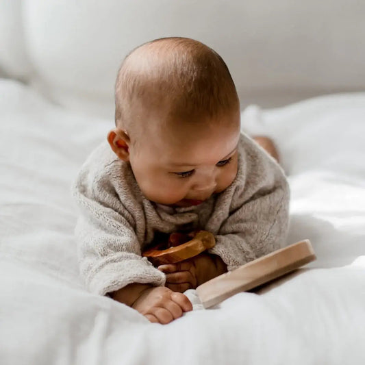 Baby playing with wooden toys on a white blanket
