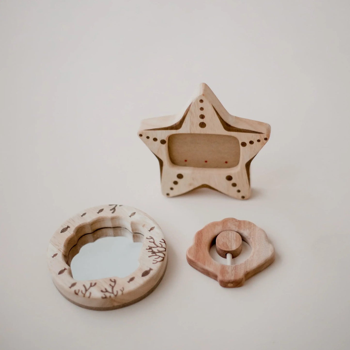 a seashell wooden rattle, a wooden seashell mirror, and a wooden starfish photo frame on a beige background