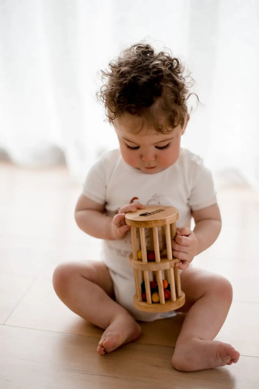 a baby sitting on a wooden floor holding a mini wooden rain maker