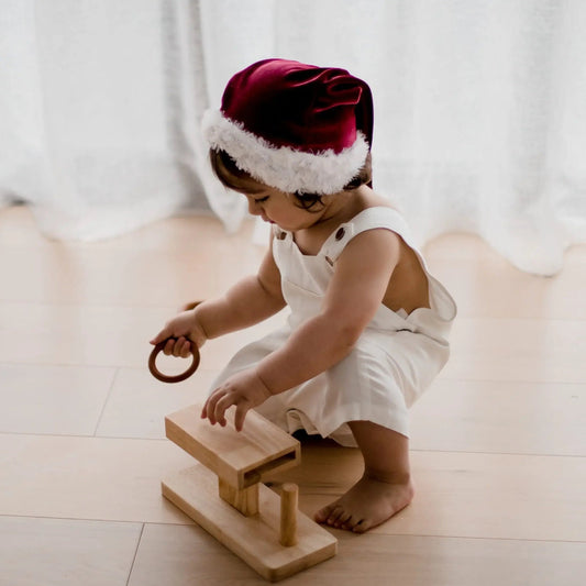 a child wearing a Santa hat and a white dress playing with a rings activity toy on the floor