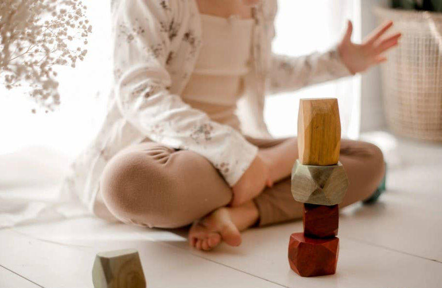 Child playing with wooden stacking gems on a light-colored floor.