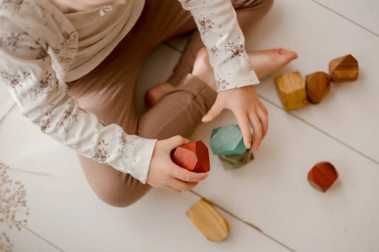 A child playing with rainbow stacking gems on a light wooden floor.