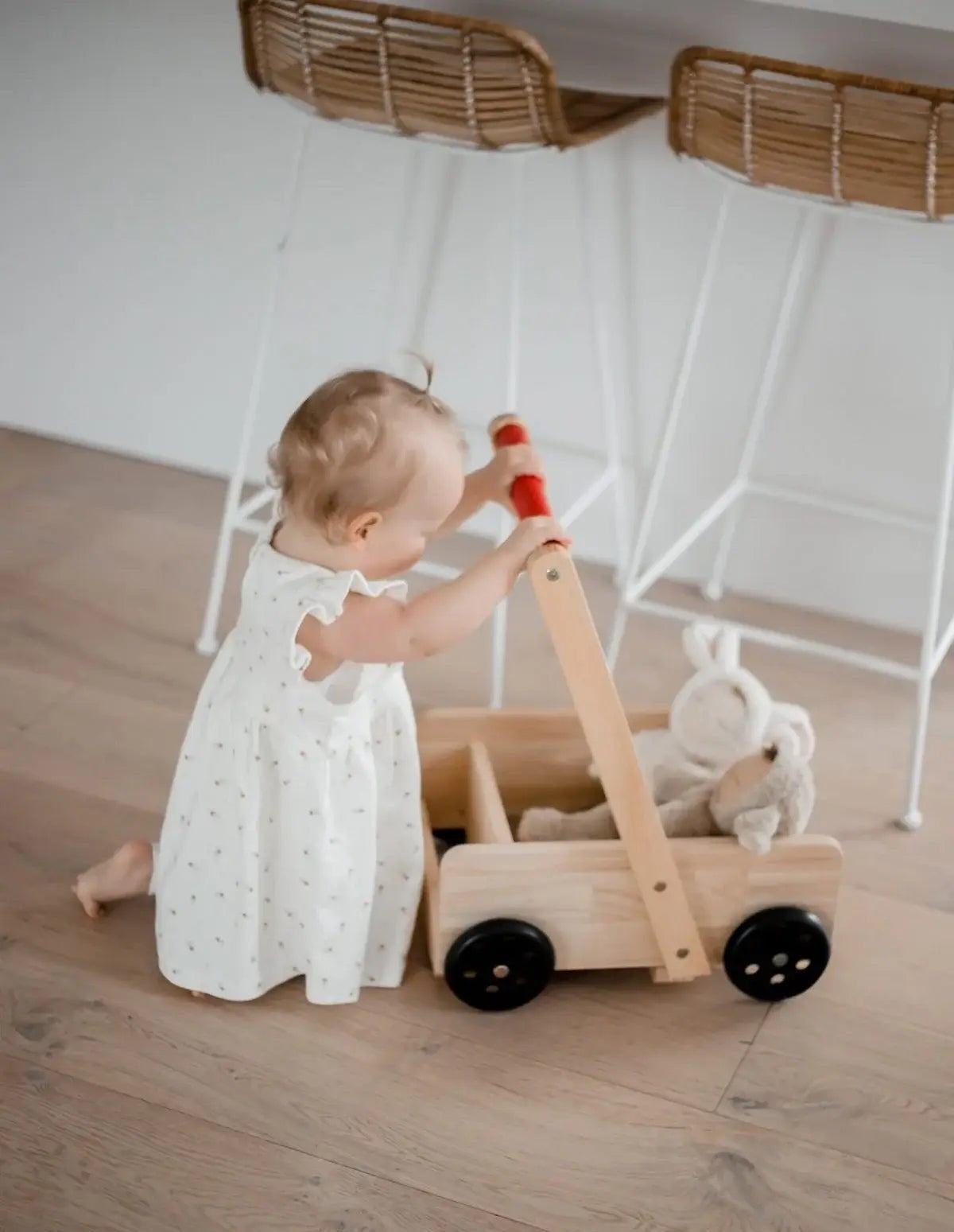 Baby playing with a wooden walker on a wooden floor.