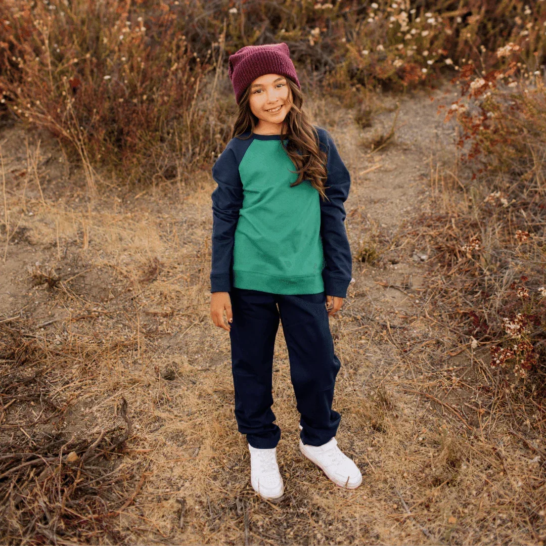 Child wearing a green and navy outfit with a maroon beanie in a natural setting