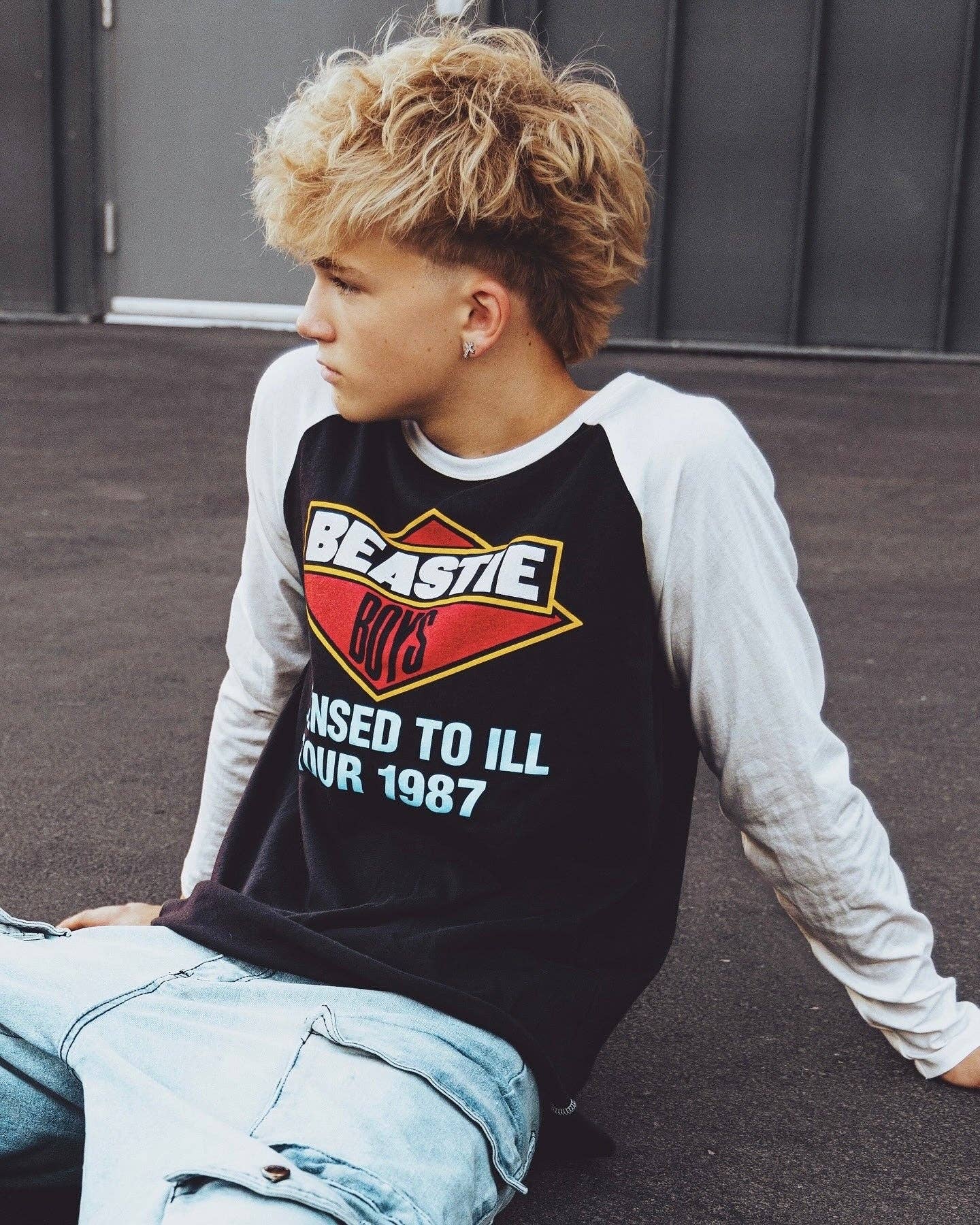 Kid wearing a black 'Beastie Boys' shirt sitting on the ground.