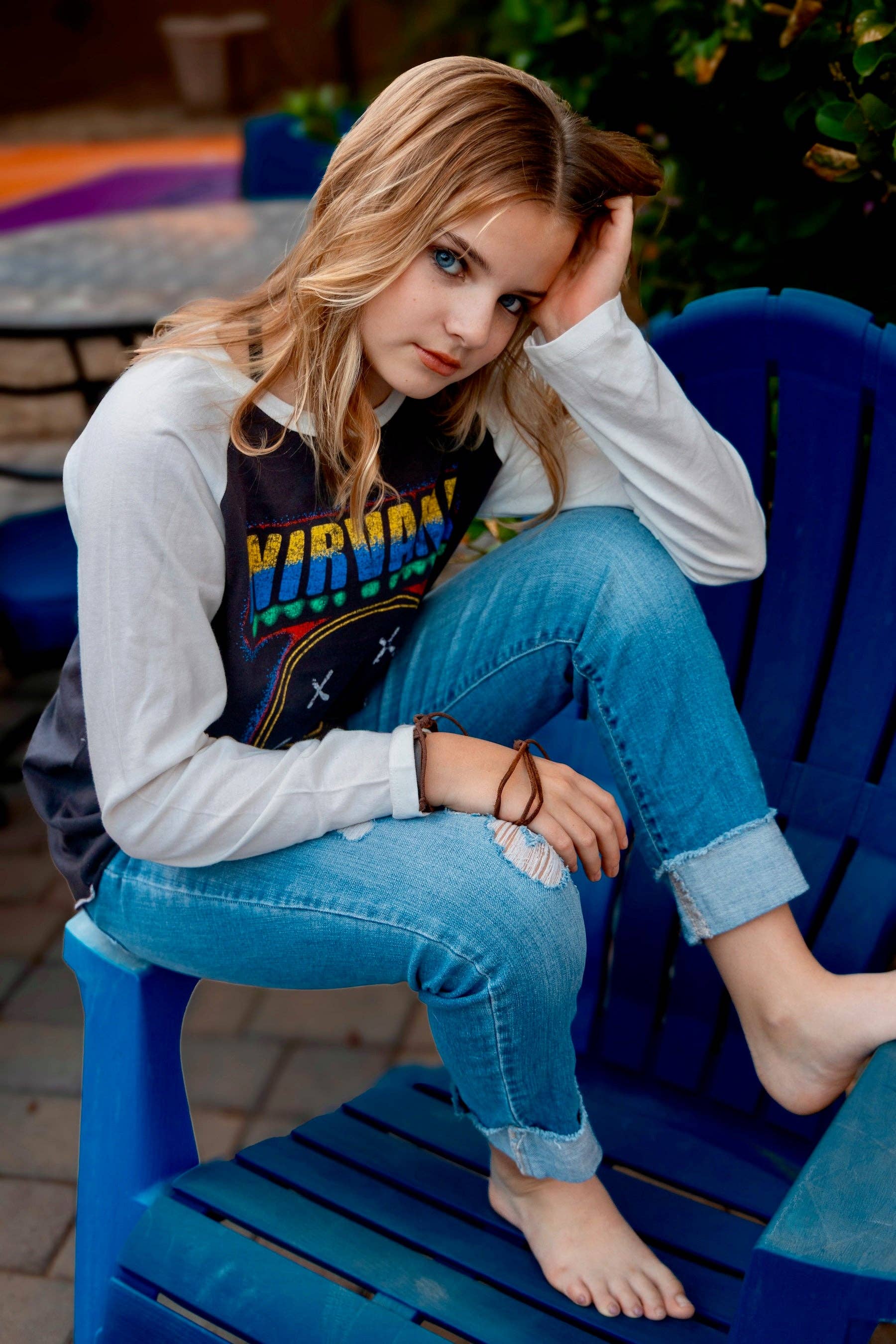 Person wearing a Nirvana shirt sitting on a blue chair outdoors.