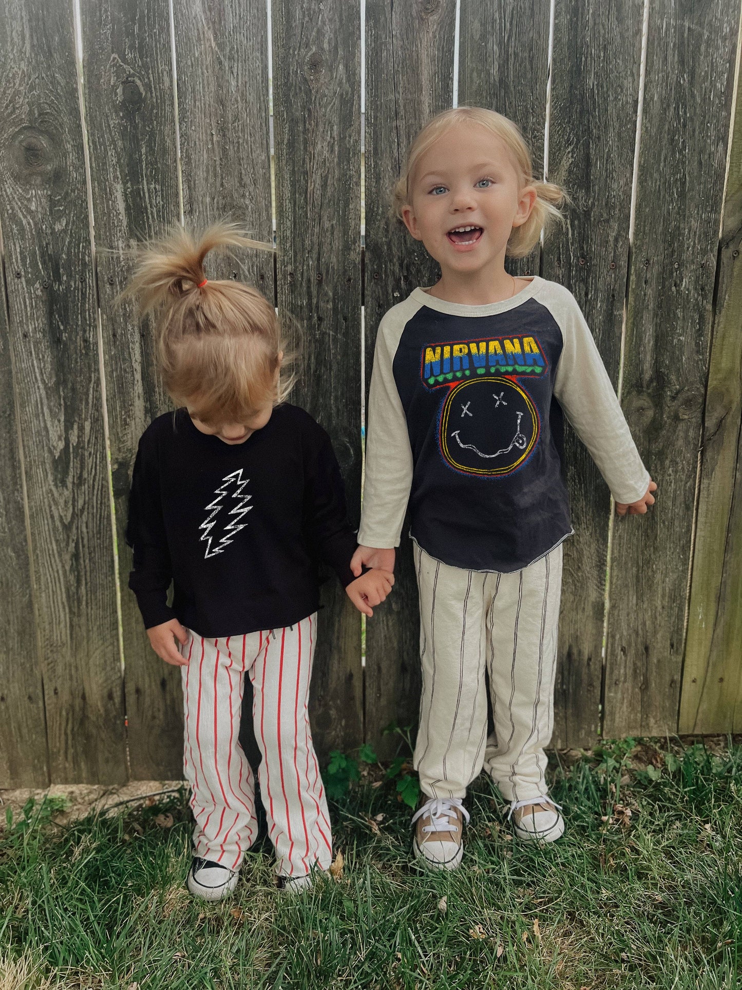 Two children standing in front of a wooden fence, wearing Nirvana-themed clothing.