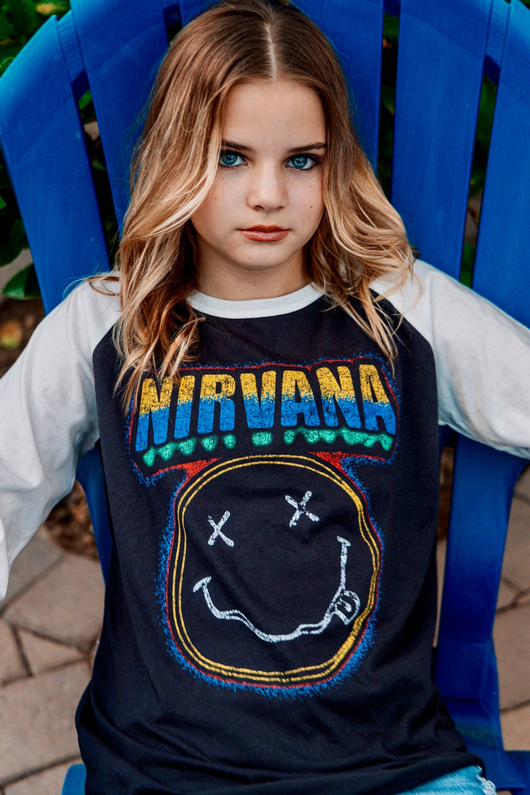 Person wearing a Nirvana t-shirt with a smiley face design, sitting on a blue chair.