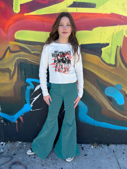 Person wearing a graphic Ramones long sleeve tee and green flared pants standing in front of a colorful mural.