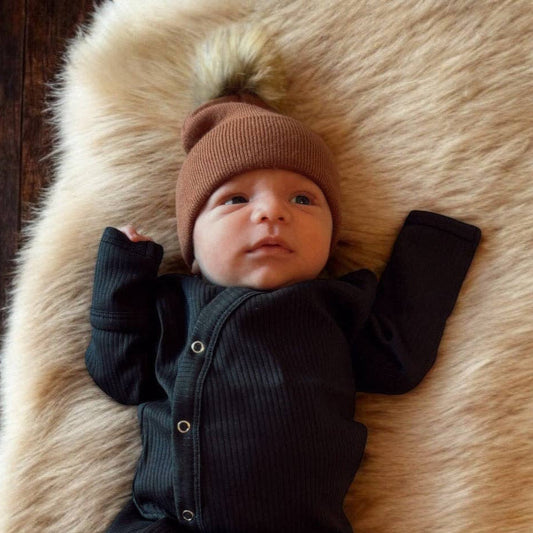 Baby in a black gown and brown hat lying on a fur rug