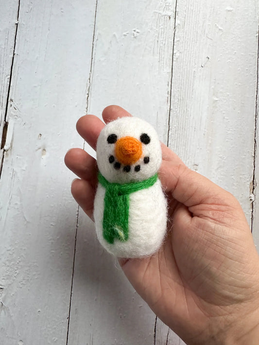 a hand holding a felt snowman with a green scarf