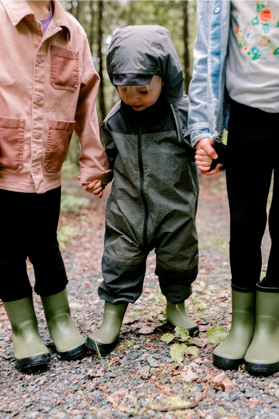 Children in rain gear holding hands  in a forest