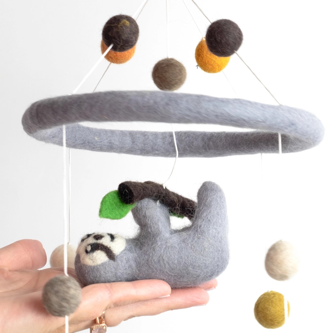 Hand holding a sloth-themed mobile with hanging felt balls against a white background