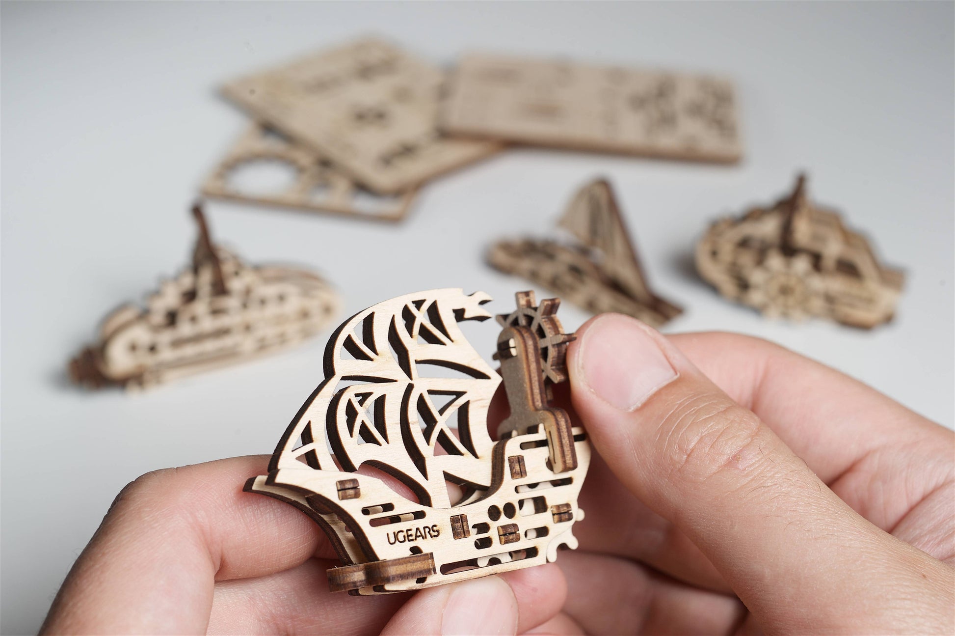 Hand holding a wooden 3D model ship with more pieces in the background on a light surface