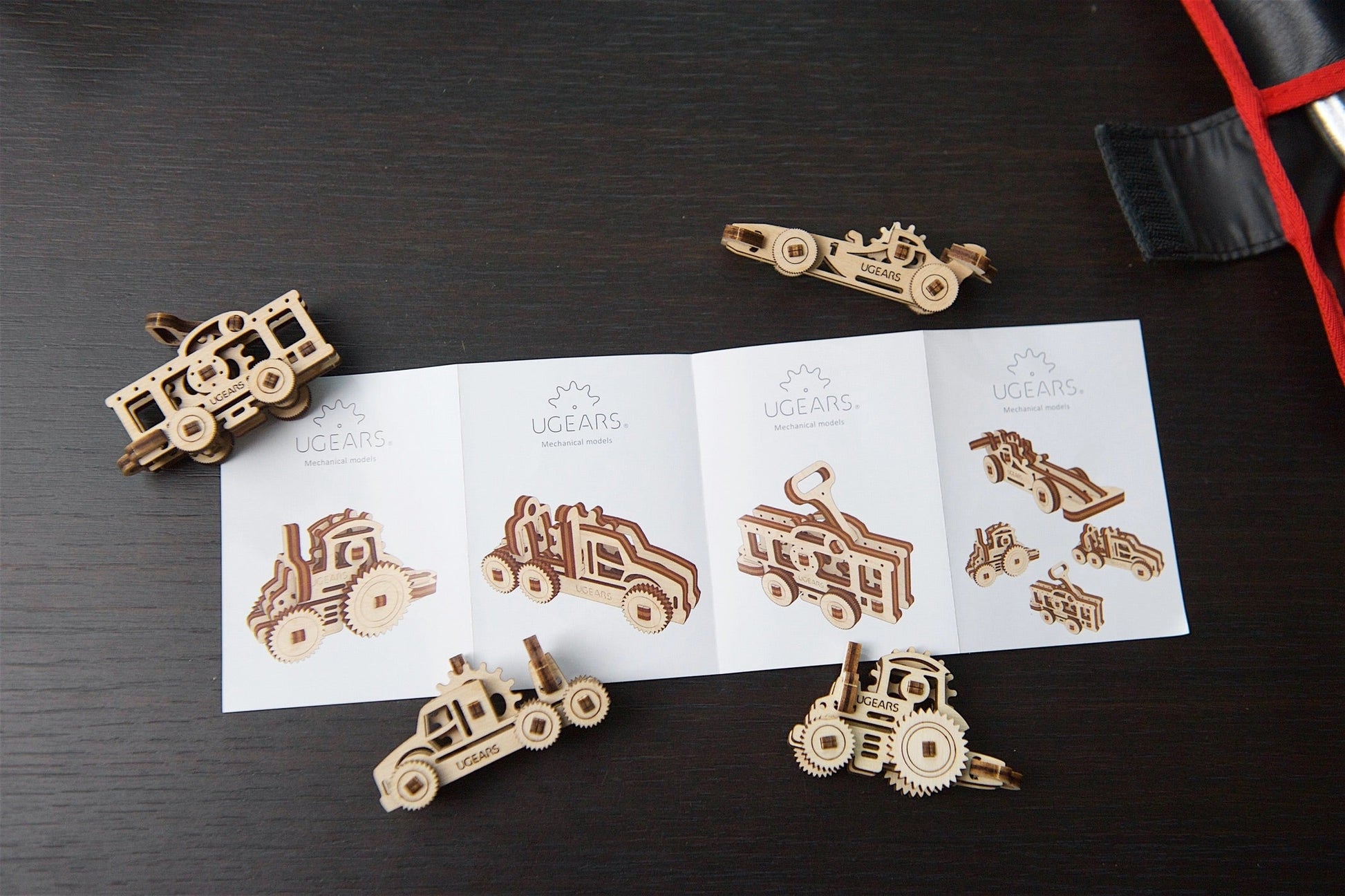 Wooden toy vehicle models on a dark surface with a sheet of printed designs.