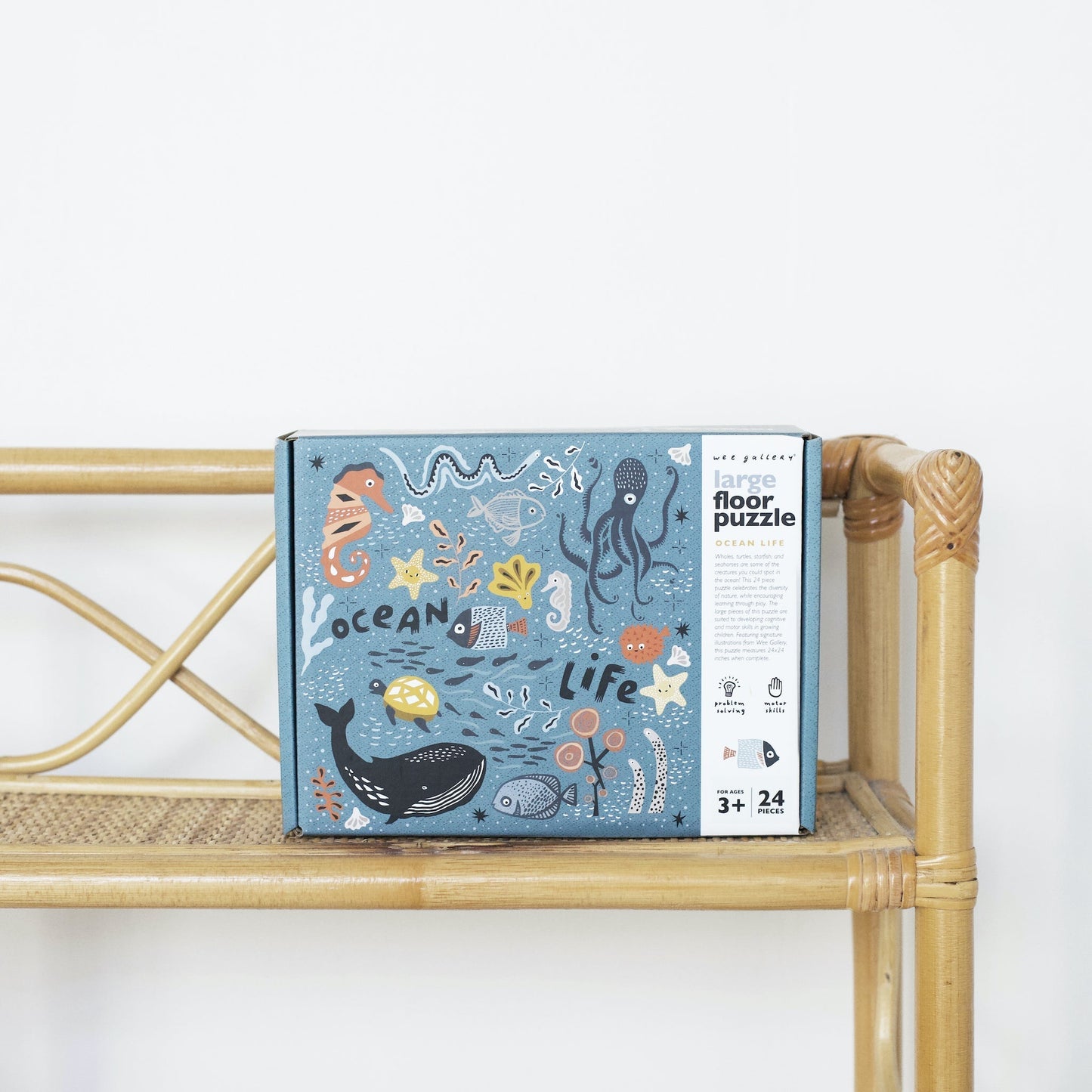 Box of an ocean-themed floor puzzle on a bamboo shelf with a white background