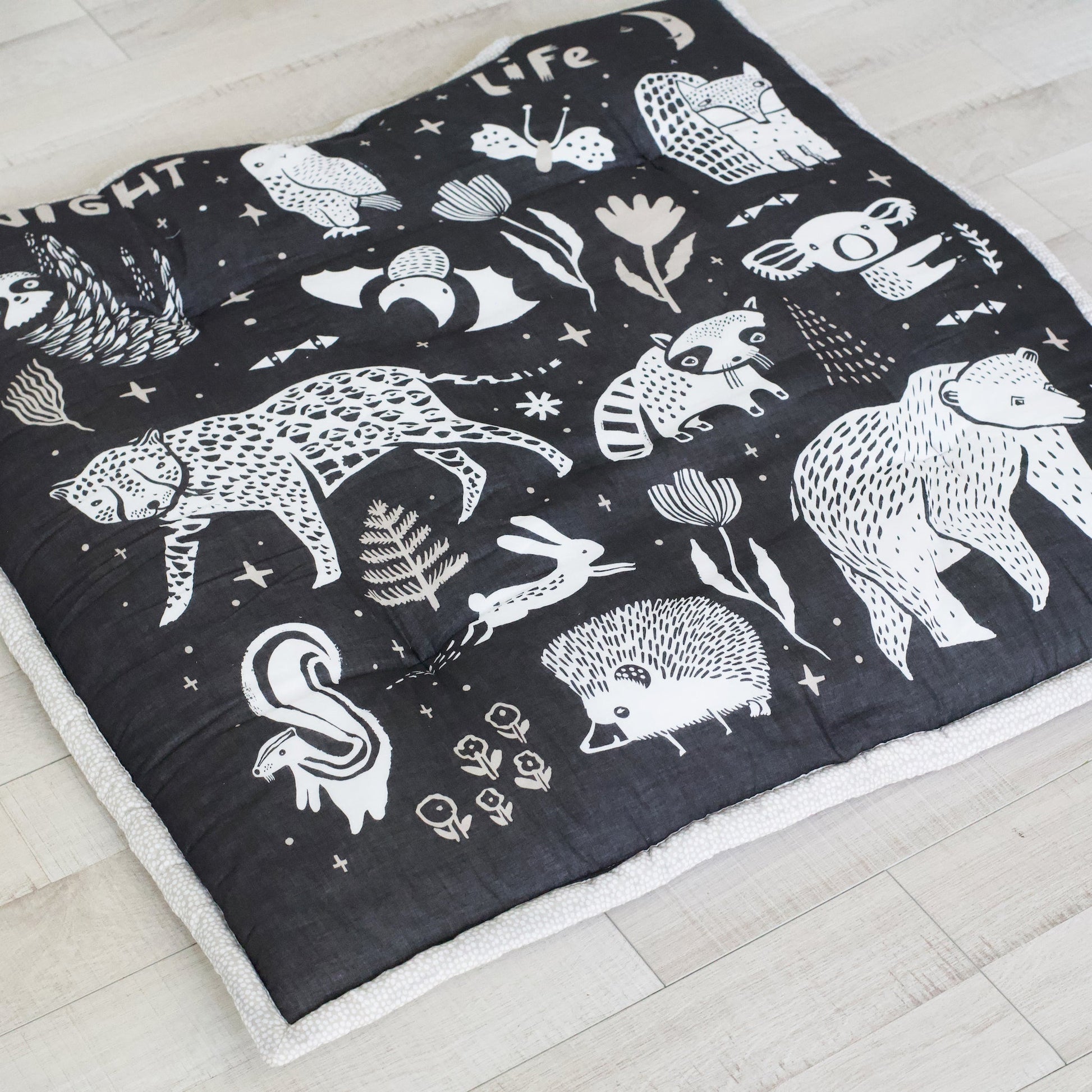 Black quilt with white animal illustrations on a light wooden floor