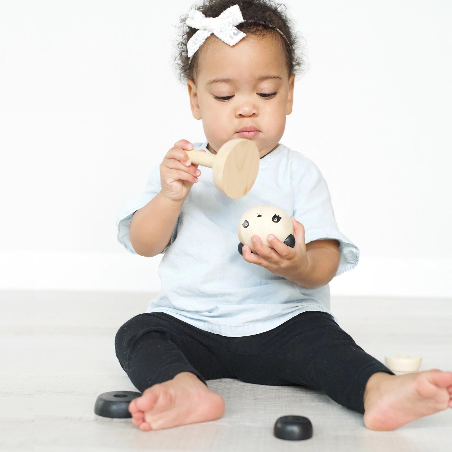 A baby sitting on the floor playing with a wooden panda stacker on a light background