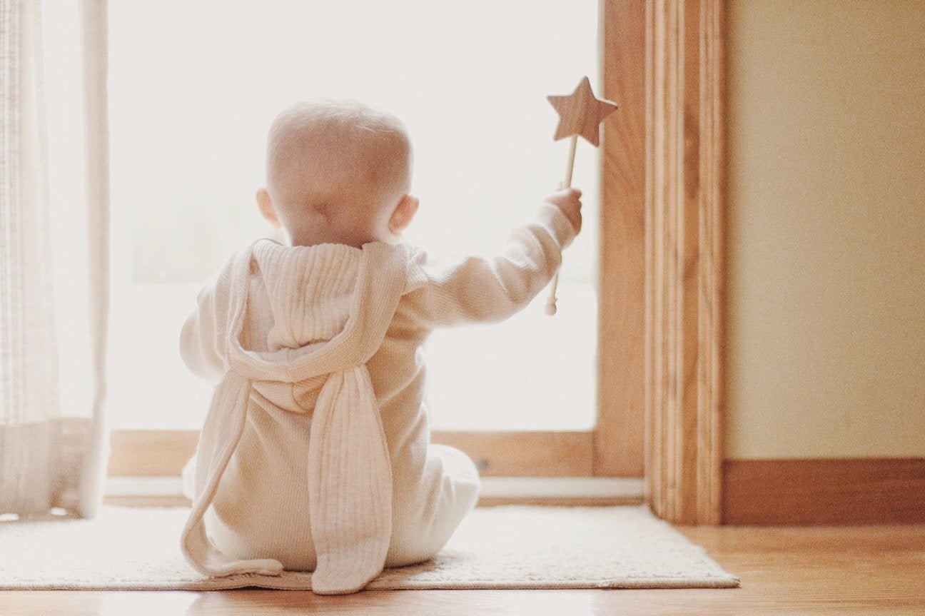 Baby sitting on a rug holding a wooden star toy in a softly lit room.