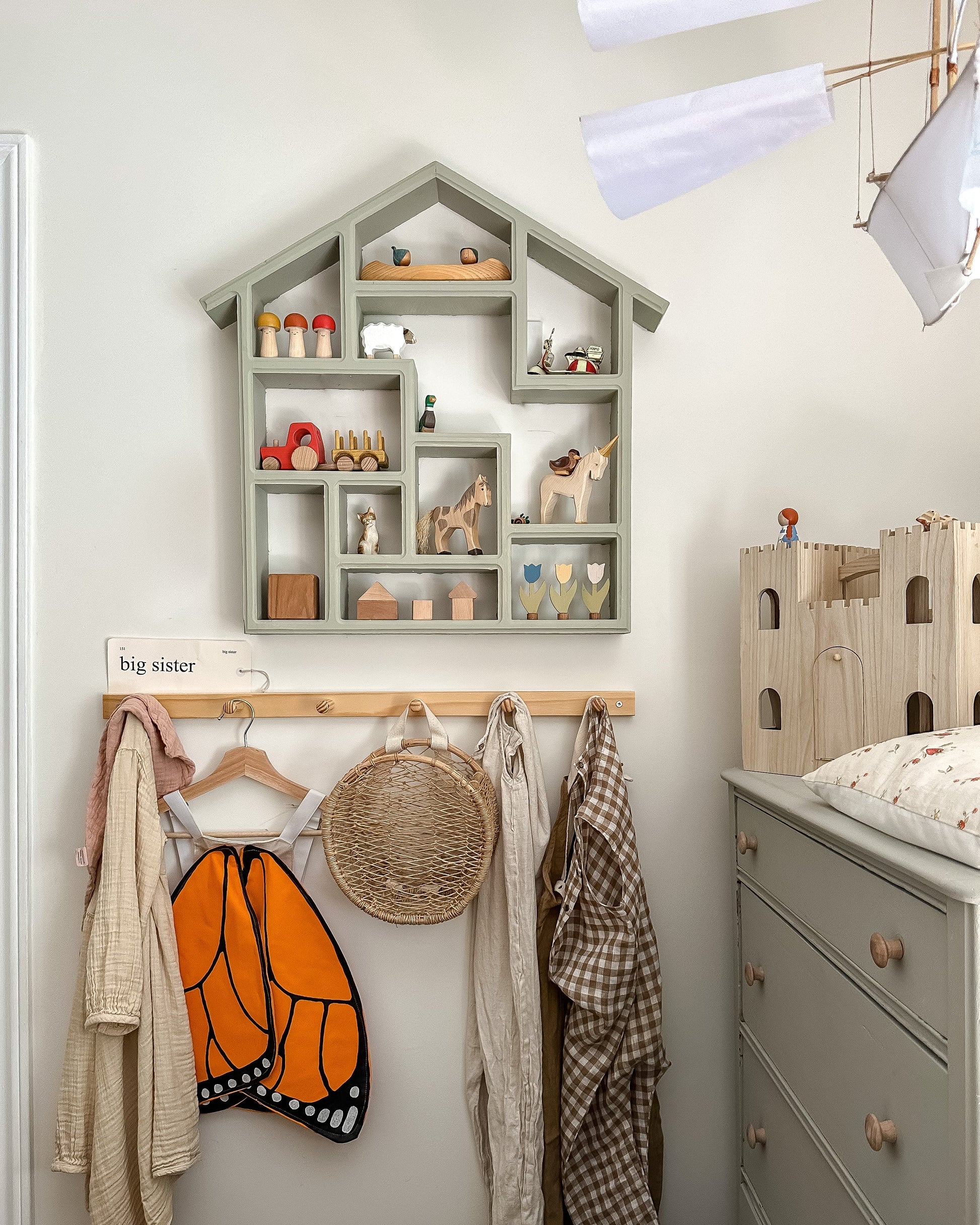 Children's room with a house-shaped shelf, clothes, and toys.