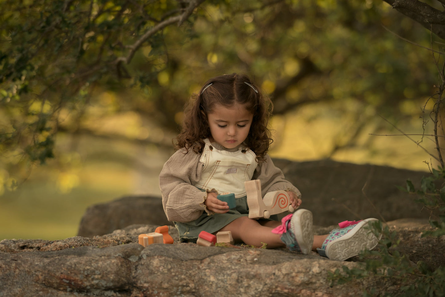 Child sitting on a rock with toys, surrounded by greenery
