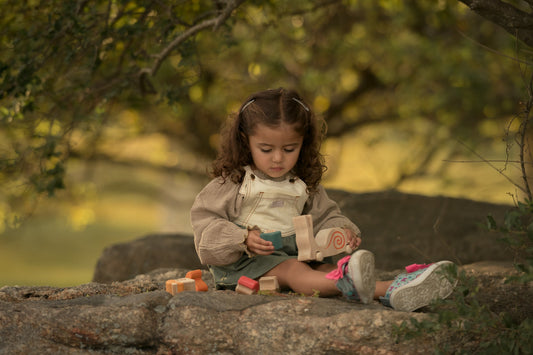 Child sitting on a rock with toys, surrounded by greenery