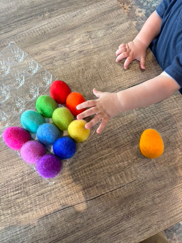 Colorful pom-poms on a wooden surface with a child's hand reaching out.
