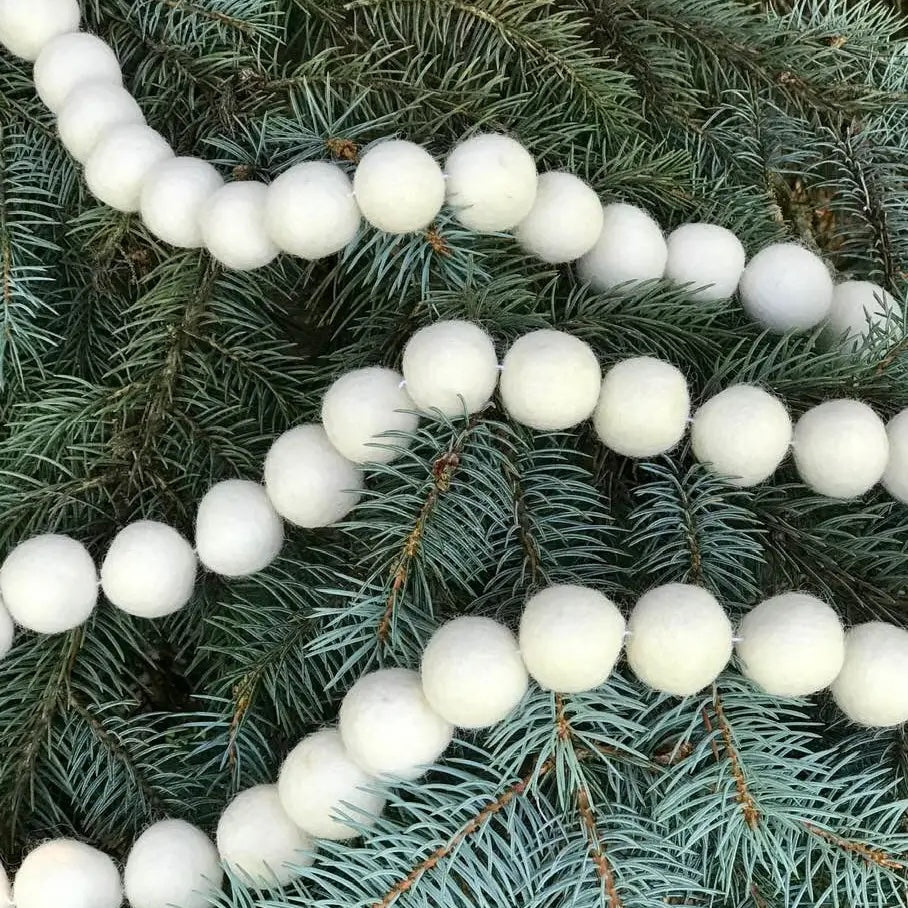 Felt ball garland in white draped on a pine tree