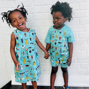 Two children standing and holding hands. One is wearing a teal dress with a colorful beetle print. The other is wearing a t-shirt and shorts with the same print.