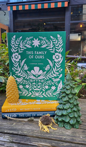 This Family of Ours by Anne Phyfe stacked on two other books with flowers and candles on a wooden table