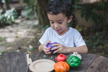 Load image into Gallery viewer, A child playing with a wooden vegetable set on a wood table outdoors. The child osopening the onion
