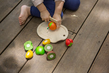 Load image into Gallery viewer, Child  outside on a deck cutting a wooden  velcro orange from the plan toys Assorted Fruit Set
