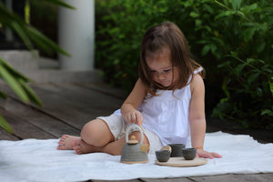 Child sitting outside playing with classic tea set by PlanToys