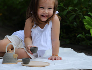 Child sitting outside playing with classic tea set by PlanToys