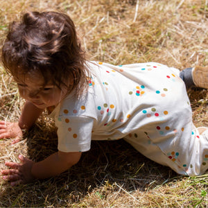 Baby crawling in a grass field wearing Rainbow Balloons Organic Summer Romper