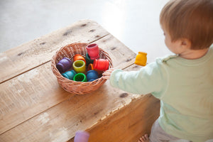 A baby playing with rainbow wooden cups in a basket.