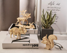 Load image into Gallery viewer, Three assembled 3D wooden puzzles on a desk, from left to right of a moose, elephant, and squirrel
