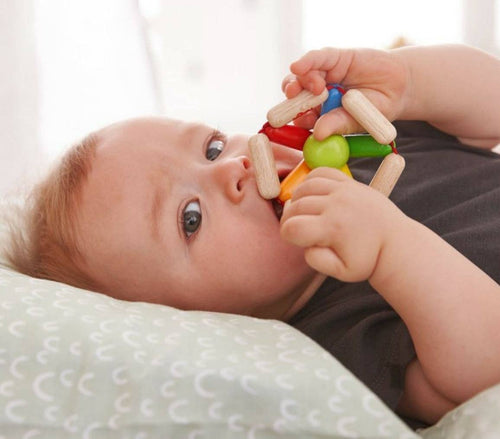 baby laying on a bed holding Color Carousel Wooden Clutching Toy