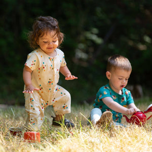 Two babies playing with a tea set in a grass field, one wearing Rainbow Balloons Organic Summer Romper