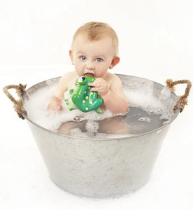 Baby taking a bath in a tin chewing on rubber frog