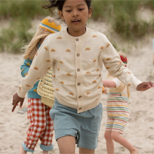 Child with brown hair running wearing bluw shorts and From One To Another Rainbows Knitted Cardigan Sweater
