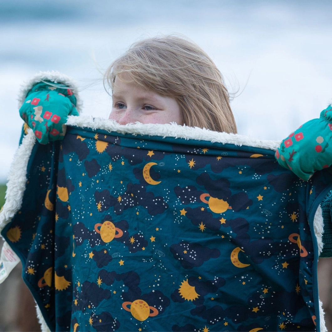 child standing outside wearing mittens and holding up a Saturn nights sherpa blanket