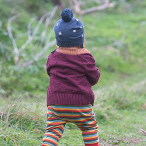child walking outside wearing a hat, sweater, and rainbow striped joggers