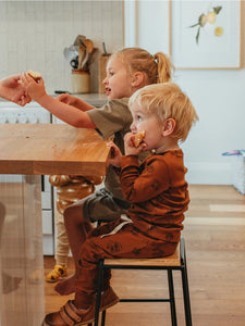Children sitting at a wooden table wearing Ziwi Baby sets