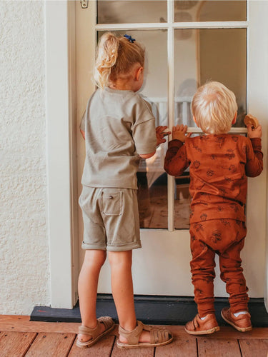 two children looking through a door wearing Ziwi Baby sets